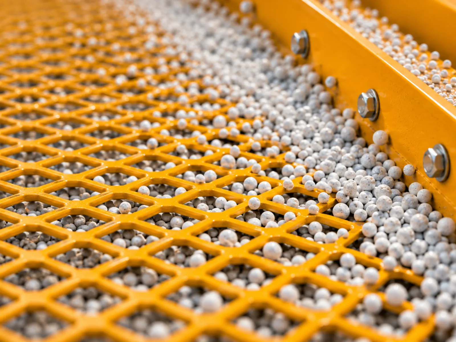 Close-up of fertilizer granules moving across an industrial screening mesh